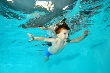 The little boy swims underwater and soars like a bird, spreading his hands on a blue background....