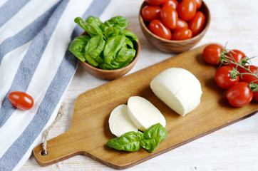 Mozzarella cheese with red tomatoes and basil leaves, pepper, olive oil, wooden desk, healthy food concept