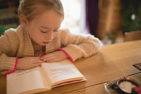 Cute girl sitting at table and reading book
