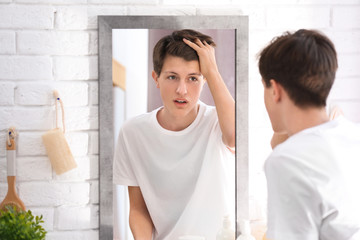 Teenage boy with acne problem looking in mirror at home