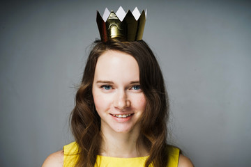 beautiful blue-eyed girl in a yellow dress smiles and looks at the camera, on her head a golden...