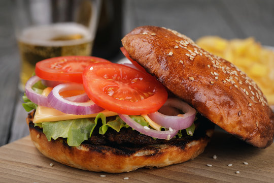 Delicious hamburger with vegetables and a cutlet. Sandwich with beer close-up