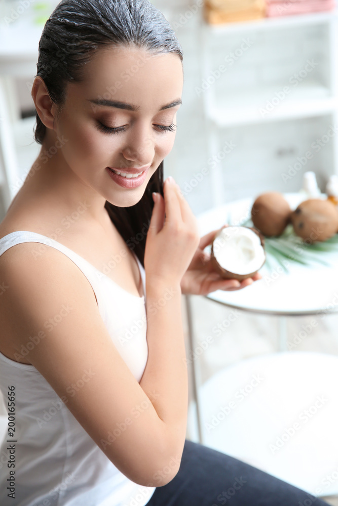 Wall mural Young woman applying coconut oil onto hair at home