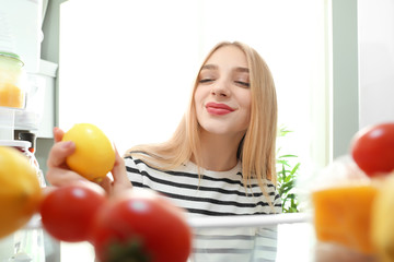 Young woman with fresh lemon near open refrigerator, view from inside