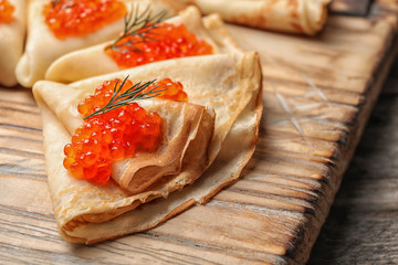 Thin pancakes with delicious red caviar on wooden board