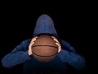 hooded basketball player holding ball in hands isolated in dark background