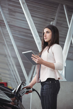 Beautiful woman using digital tablet while charging electric car