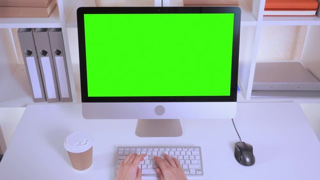 top view invisible woman working on computer. female typing on white keyboard using pc mouse. workplace with white table folders monitor with isolated green screen