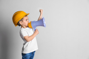 Adorable little boy in hardhat with megaphone on light background