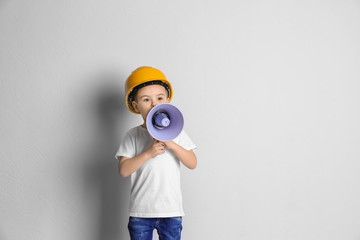 Adorable little boy in hardhat with megaphone on light background