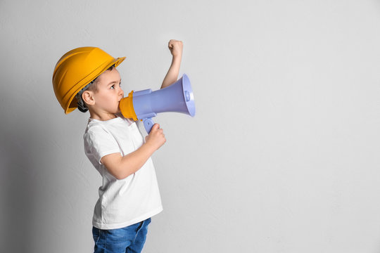 Adorable little boy in hardhat with megaphone on light background