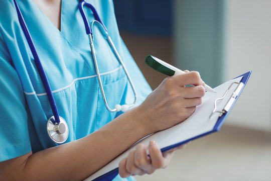 Mid Section Of Nurse Writing On Clipboard