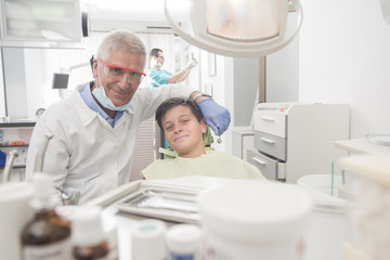 Boy with perfect teeth at the dentist doing check up while other doctors analyze x-ray in the background - oral hygiene health care concept