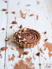 Chocolate tarts served with almond nuts on shabby white wooden surface