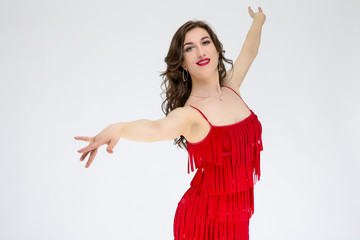 Ballroom Dances Project and Ideas. Portrait of Female Ballroom Dancer in Red Flowing Latin American Dress Against White. Demonstrating Rumba Dance.