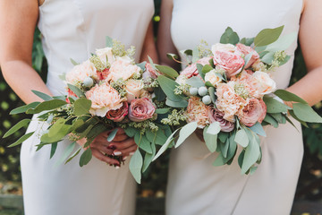 Two bridesmaids wearing white dresses holding their bouquets with peonies and eucalyptus
