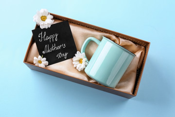 Gift box with cup and greeting card for Mother's day on color background