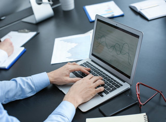 Man working with laptop in office, closeup. Forex concept