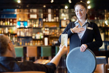 A girl waitre gets a tip from the client in the bar of the hotel. The girl in the vow. Emotions. The concept of service.