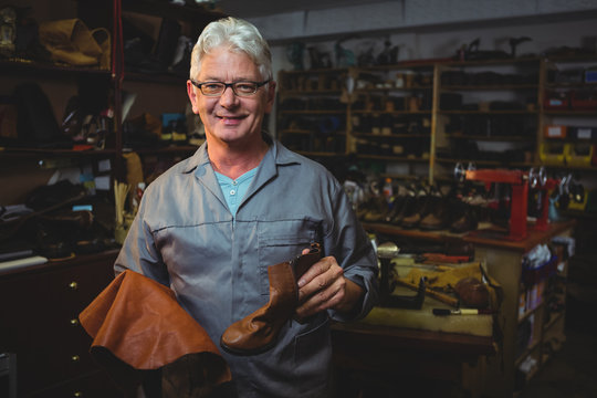 Portrait of smiling cobbler with shoe standing in workshop