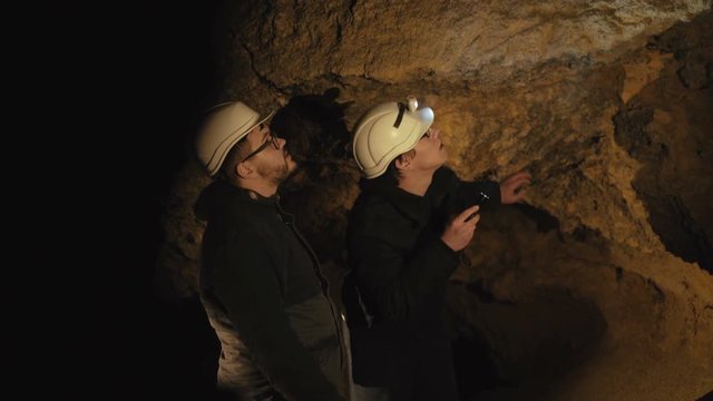 Two speleologists with flashlight exploring the cave with fear in darkness
