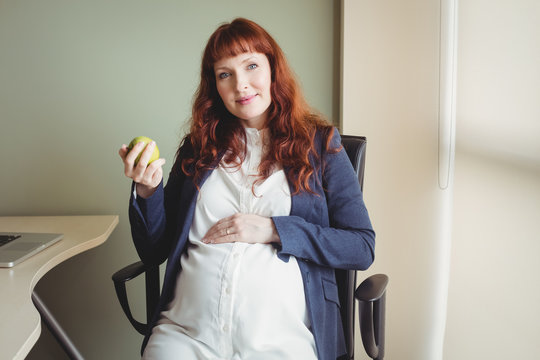 Portrait of pregnant businesswoman holding an apple - Powered by Adobe
