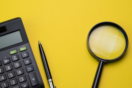 Expense, cost, budget, tax or investment calculation, flat lay or top view of black pen with calculator and magnifying glass on vivid yellow background table with copy space