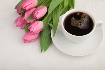 Obraz na płótnie Canvas Black coffee in white Cup with pink tulips on light stone background. Top view with copy space