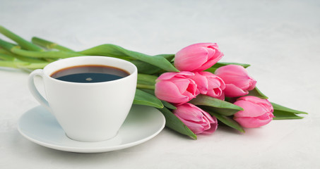 Fototapeta na wymiar Black coffee in white Cup with pink tulips on light stone background