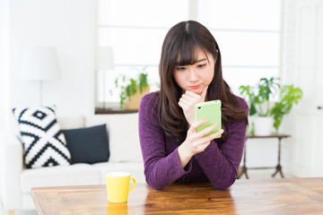 部屋でスマホを見る女性　考える