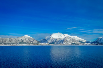 Fototapeta na wymiar Amazing landscape of coastal scenes of huge mountain covered with snow on Hurtigruten during voyage in a blue sky