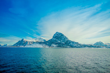 Outdoor view of coastal scenes of huge mountains partial covered with snow durig a trip in Hurtigruten in a blue sky