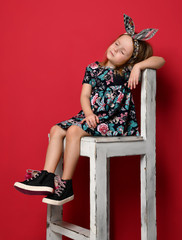 Cute baby girl kid in fashion summer dress and headband sitting on chair thinking