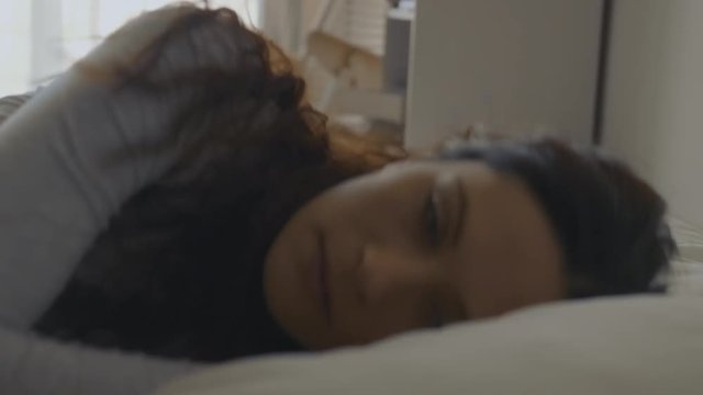 Close-up shot of a pensive woman turning in bed showing her face.

