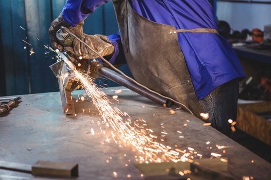 Worker grinding metal with grinder in workshop