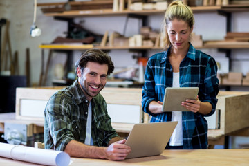 Male and female carpenters using digital tablet and laptop