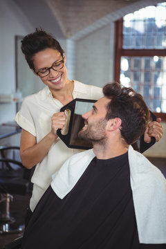 Female hairdresser showing man his haircut in mirror at salon