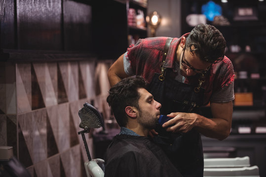 Barber shaving man's beard with trimmer in barber shop