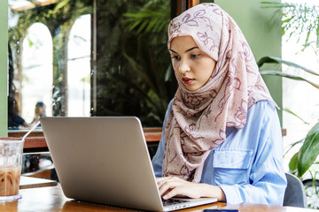 Islamic woman sitting and using laptop - obrazy, fototapety, plakaty