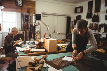 Attentive craftswoman cutting leather