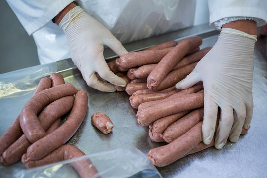 Butcher packing raw sausages in meat factory
