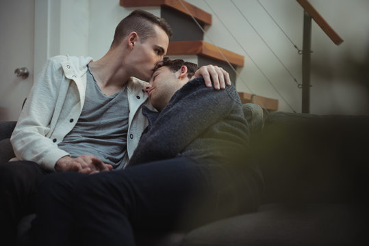 Gay man kissing his partner while sitting on sofa at home