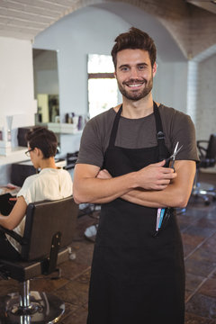 Male hairdresser standing with arm crossed at a salon
