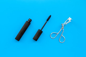 Basic products for eyelashes makeup. Mascara and eyelash curler on blue background top view copy space