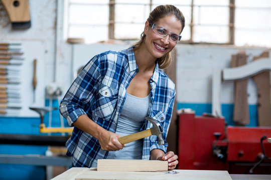 Female carpenter holding a hammer to drive nail into a wooden plank