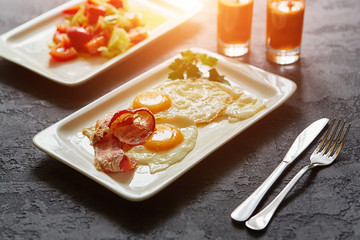 Breakfast from fried egg, bacon, vegetable salad and carrot juice. On a dark stone background
