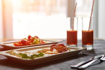Breakfast from fried egg, bacon, vegetable salad and carrot juice. On a dark stone background