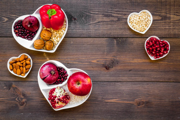 Food which help heart stay healthy. Vegetables, fruits, nuts in heart shaped bowl on dark wooden...