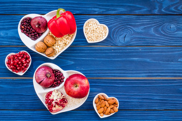 Food which help heart stay healthy. Vegetables, fruits, nuts in heart shaped bowl on blue wooden background top view copy space