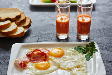 Daily Breakfast. Fried egg with bacon, carrot juice, vegetable salad, bread. On dark stone background